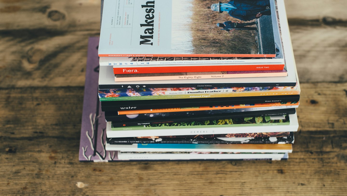 Stack of colorful magazines on a wooden table.