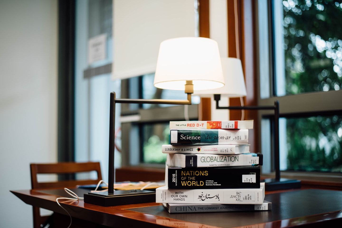 Stacked academic books on a polished wooden desk.